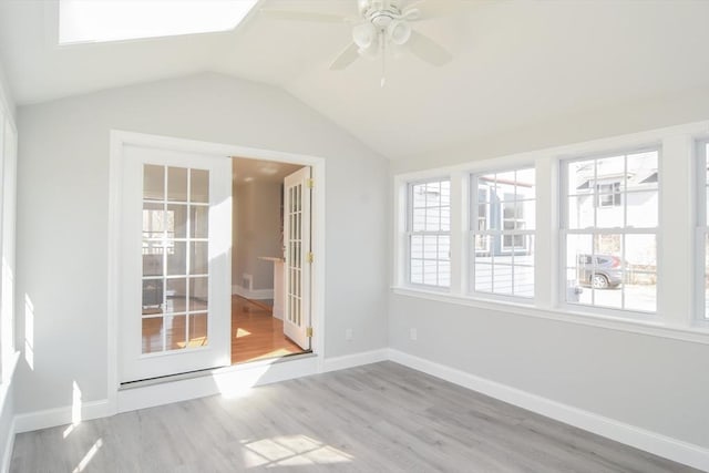 interior space with baseboards, lofted ceiling with skylight, wood finished floors, and a ceiling fan