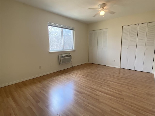 unfurnished bedroom featuring light wood-type flooring, two closets, a wall mounted air conditioner, and baseboards