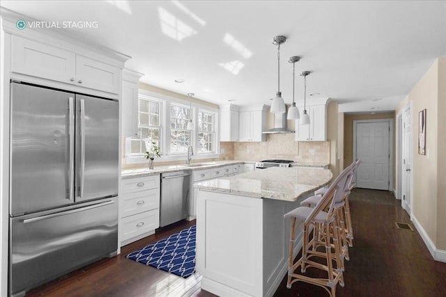 kitchen with stainless steel appliances, a center island, white cabinetry, and wall chimney range hood