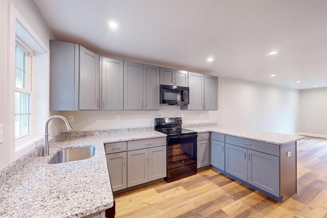 kitchen featuring black appliances, sink, light hardwood / wood-style flooring, light stone countertops, and kitchen peninsula