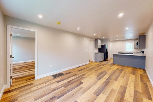 kitchen with gray cabinetry, black refrigerator, light wood-type flooring, and kitchen peninsula