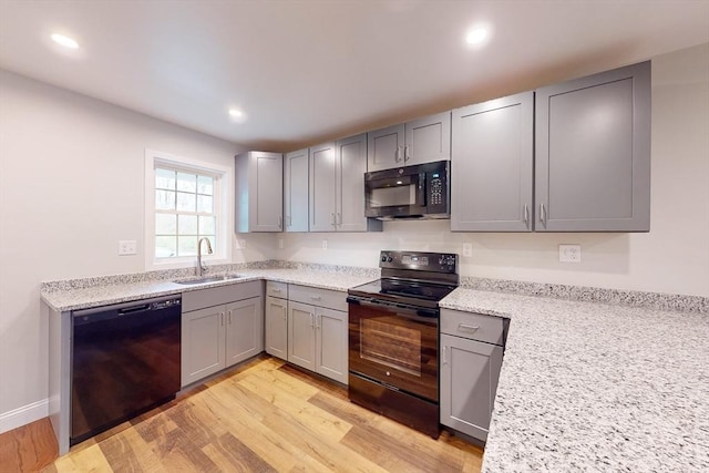 kitchen featuring light stone counters, gray cabinetry, sink, black appliances, and light hardwood / wood-style flooring