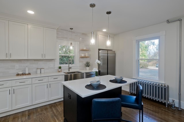 kitchen featuring white cabinets, a kitchen island, appliances with stainless steel finishes, radiator, and sink