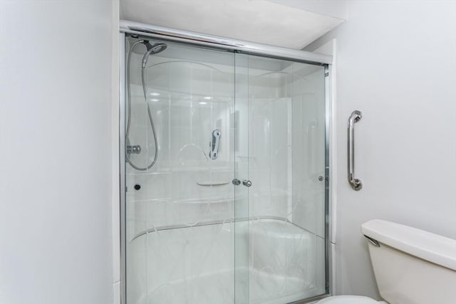 bathroom featuring a shower with door and toilet