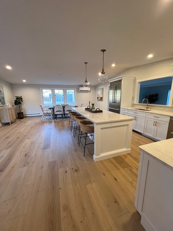 kitchen featuring white cabinetry, built in fridge, a wall mounted AC, pendant lighting, and light hardwood / wood-style floors