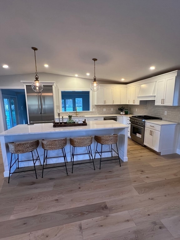 kitchen with a kitchen breakfast bar, light hardwood / wood-style flooring, white cabinetry, and high quality appliances