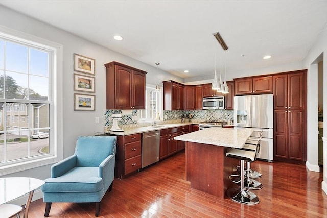 kitchen featuring a breakfast bar area, a sink, appliances with stainless steel finishes, tasteful backsplash, and dark wood-style floors