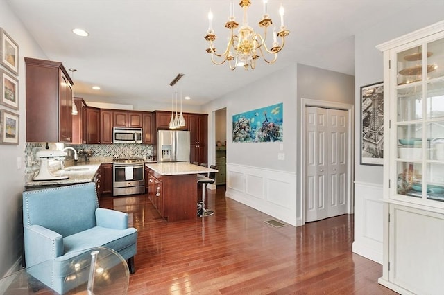 kitchen featuring a sink, stainless steel appliances, a kitchen breakfast bar, dark wood-type flooring, and visible vents