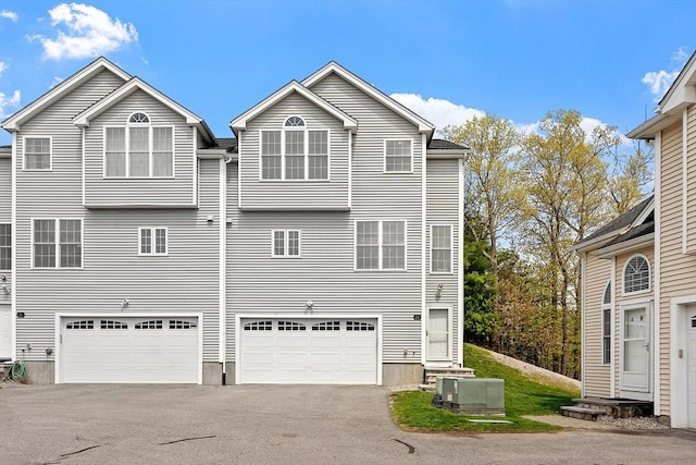 rear view of property featuring central AC unit, aphalt driveway, and an attached garage