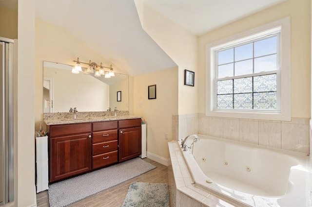 bathroom with lofted ceiling, a sink, double vanity, wood finished floors, and a tub with jets