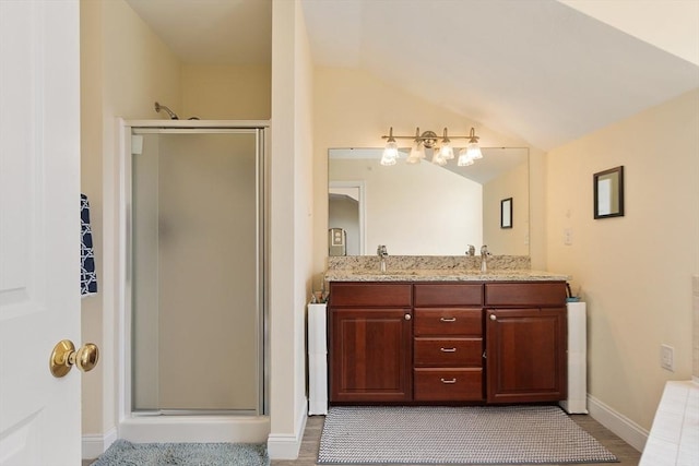 full bathroom with a sink, lofted ceiling, a shower stall, double vanity, and baseboards
