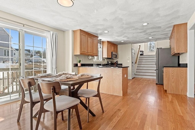 kitchen with stainless steel appliances, kitchen peninsula, a textured ceiling, and light wood-type flooring