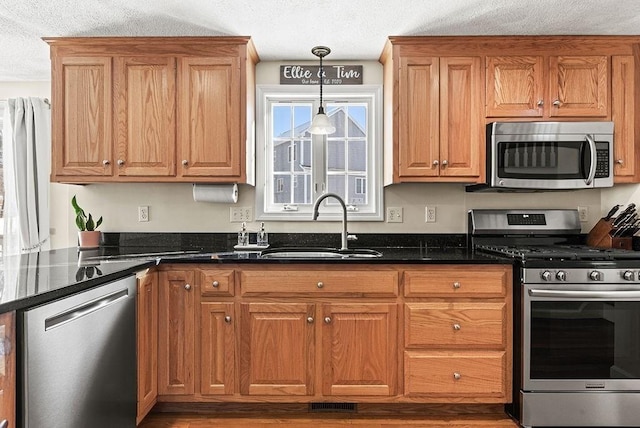 kitchen featuring dark stone countertops, sink, pendant lighting, and appliances with stainless steel finishes