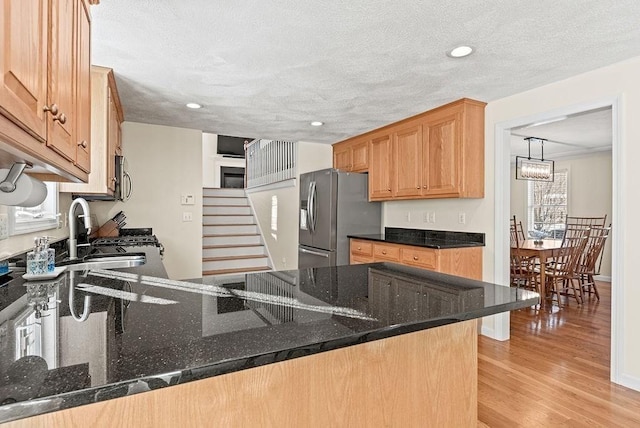 kitchen featuring sink, light hardwood / wood-style flooring, dark stone countertops, appliances with stainless steel finishes, and kitchen peninsula