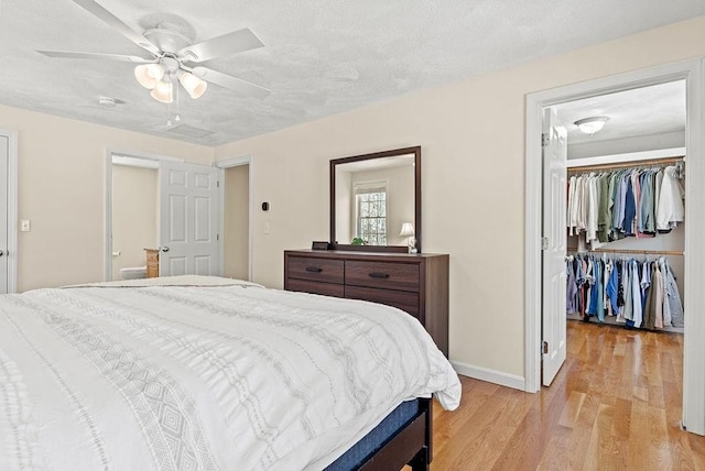 bedroom featuring a spacious closet, light hardwood / wood-style flooring, a textured ceiling, a closet, and ceiling fan