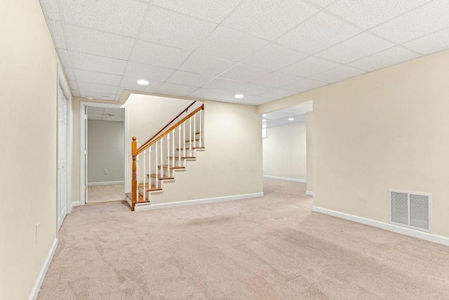 basement with a paneled ceiling and light carpet