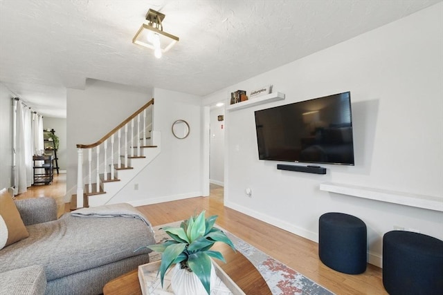 living room featuring a textured ceiling, stairs, baseboards, and wood finished floors