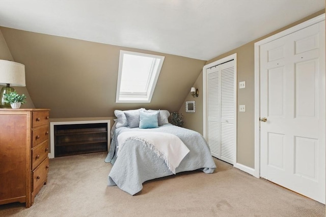 bedroom with light carpet, lofted ceiling with skylight, a closet, and baseboards