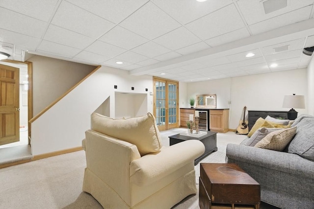 living room with a drop ceiling, light colored carpet, beverage cooler, baseboards, and stairs