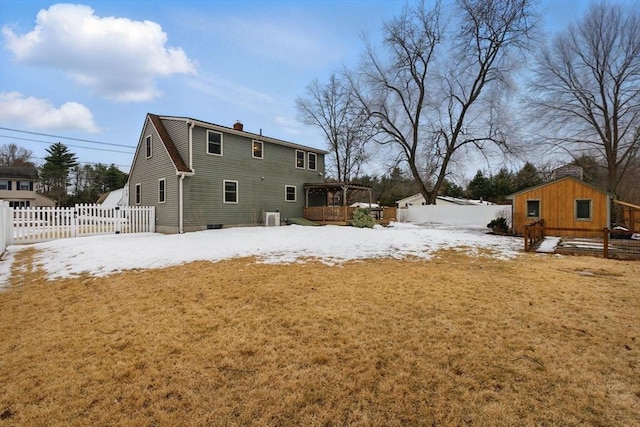 snow covered property featuring a chimney, fence, a lawn, and an outbuilding