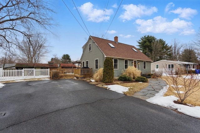 view of front facade with a shingled roof, a chimney, a wooden deck, and fence