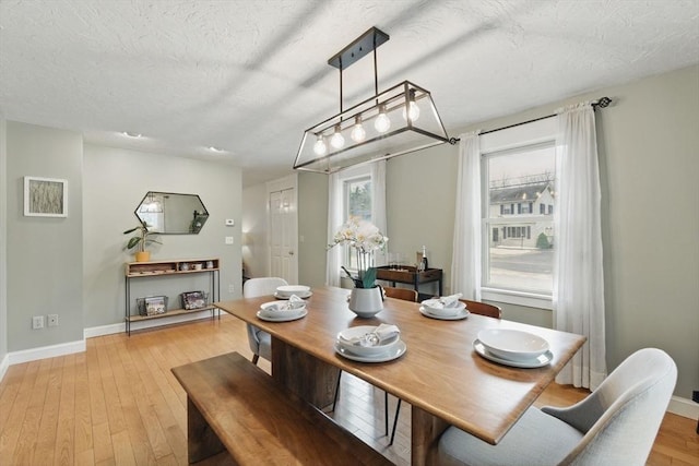 dining room with a textured ceiling, light wood finished floors, and baseboards