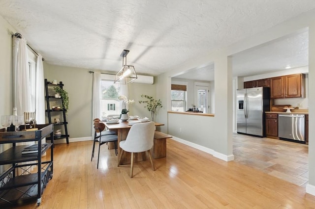 dining area with light wood-type flooring, baseboards, a textured ceiling, and a wall mounted air conditioner