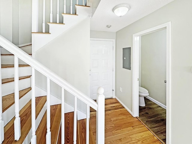 staircase with a textured ceiling, wood finished floors, electric panel, and baseboards