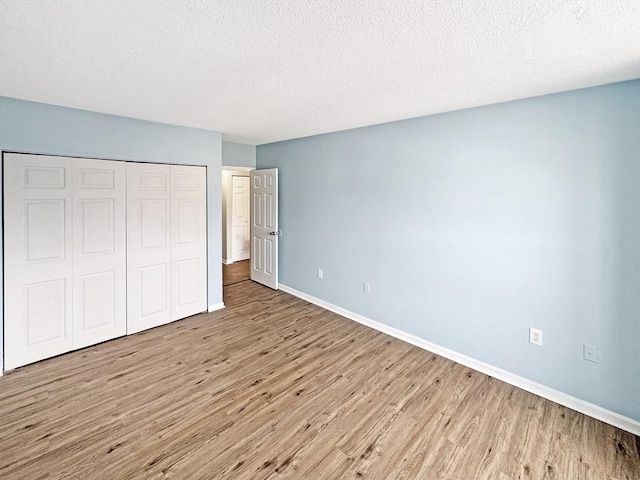 unfurnished bedroom with a closet, a textured ceiling, baseboards, and wood finished floors