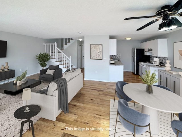 living area featuring light wood-style floors, ceiling fan, stairs, and baseboards