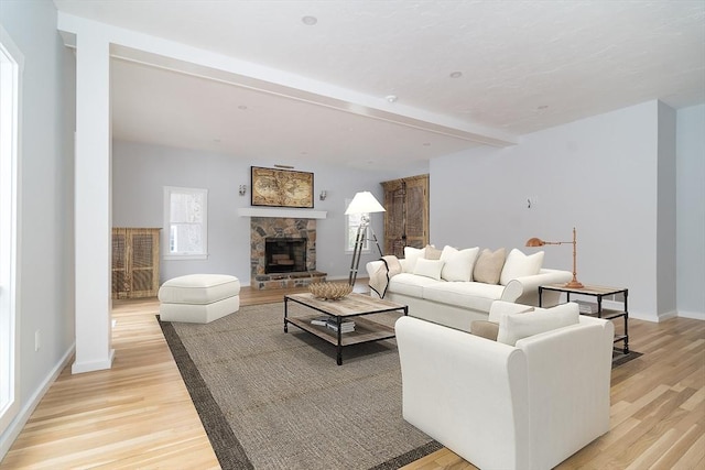 living room featuring a stone fireplace, light hardwood / wood-style flooring, and beam ceiling