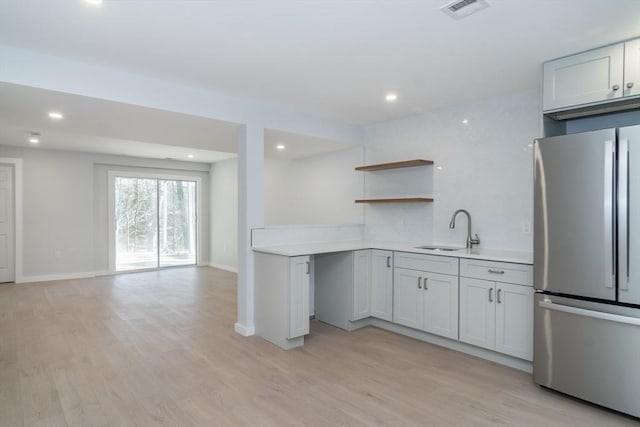 kitchen featuring white cabinets, light wood-type flooring, stainless steel fridge, sink, and backsplash