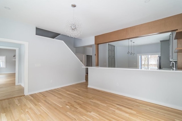 unfurnished living room with sink, an inviting chandelier, and light hardwood / wood-style flooring