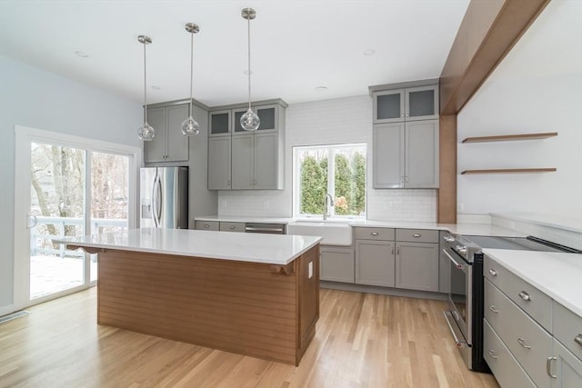 kitchen featuring gray cabinets, stainless steel appliances, a center island, sink, and backsplash