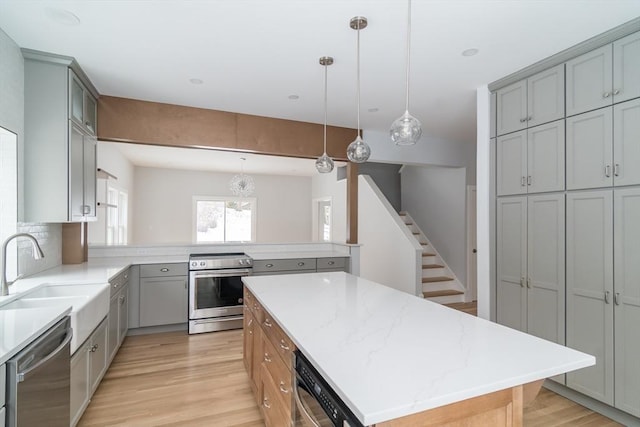 kitchen with light stone counters, decorative light fixtures, a kitchen island, appliances with stainless steel finishes, and sink