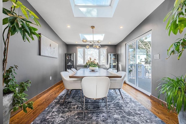 dining room with baseboards, wood finished floors, a skylight, and a chandelier