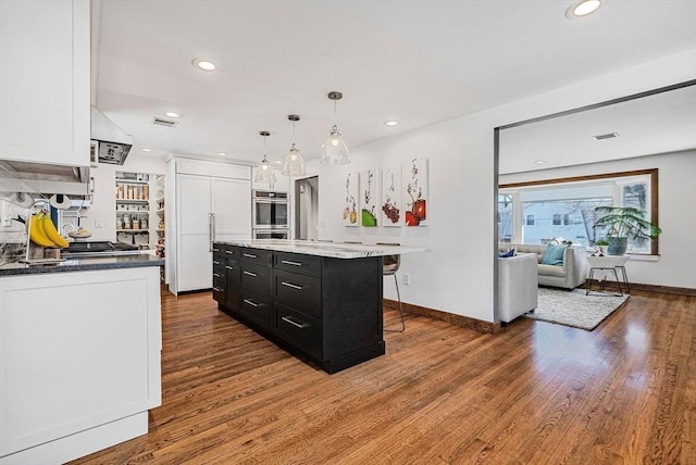 kitchen featuring a breakfast bar, wood finished floors, dark cabinetry, paneled built in fridge, and white cabinets