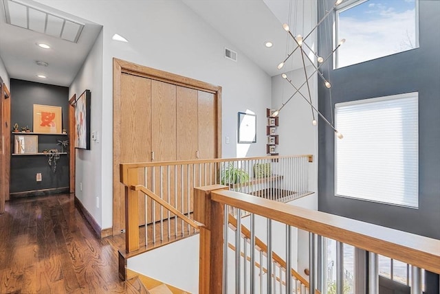 hallway with visible vents, baseboards, an upstairs landing, wood finished floors, and high vaulted ceiling