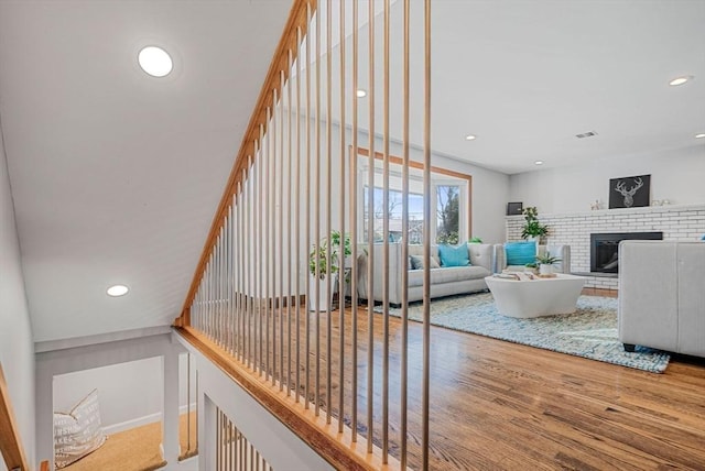 stairway with visible vents, recessed lighting, a brick fireplace, and wood finished floors