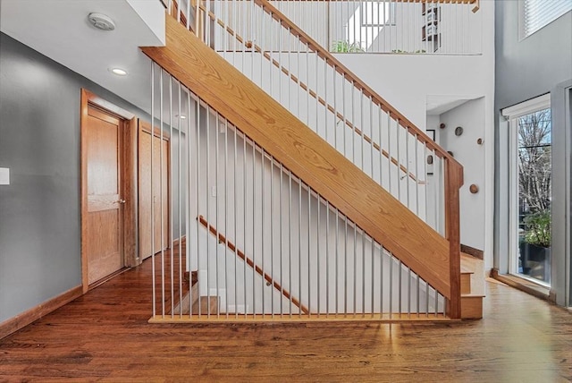 staircase with a high ceiling, wood finished floors, and baseboards