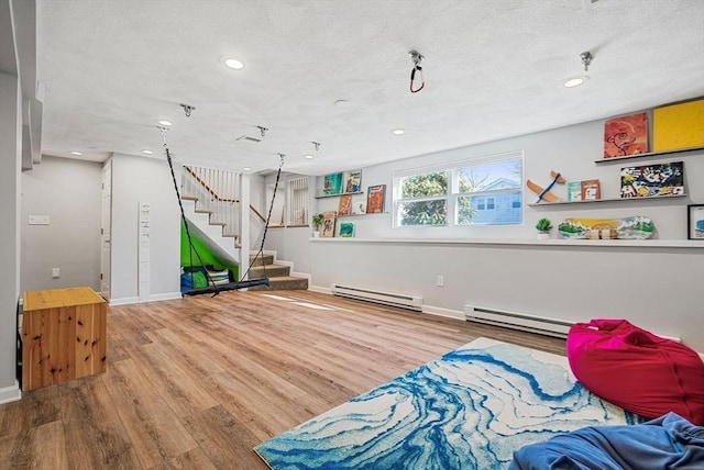 recreation room featuring a textured ceiling, wood finished floors, baseboards, and a baseboard radiator