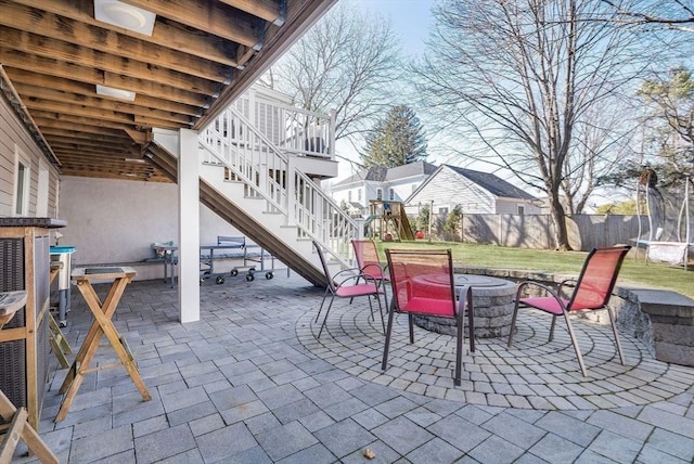 view of patio / terrace featuring stairway, fence, outdoor dining area, a fire pit, and a trampoline