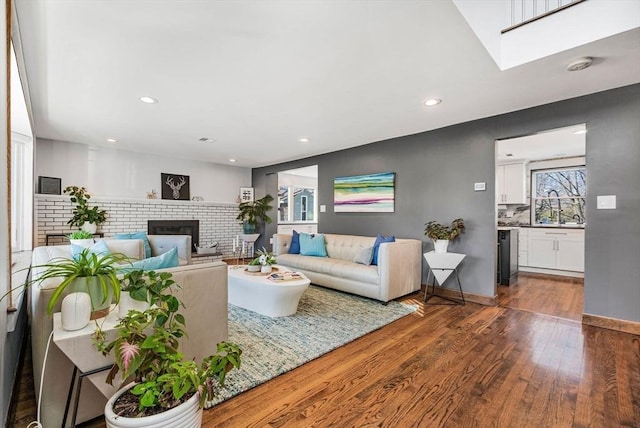 living room with recessed lighting, a brick fireplace, and dark wood-type flooring