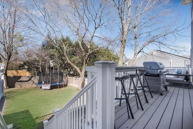 deck featuring a trampoline, a fenced backyard, a yard, and grilling area