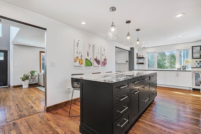 kitchen featuring pendant lighting, a breakfast bar, wood finished floors, dark cabinetry, and a center island