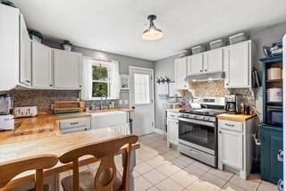 kitchen featuring light tile patterned floors, stainless steel electric range, light countertops, under cabinet range hood, and backsplash