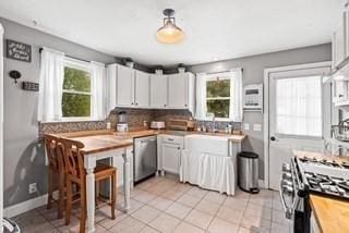 kitchen featuring tasteful backsplash, gas range, light tile patterned flooring, wood counters, and stainless steel dishwasher