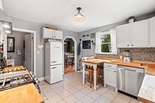 kitchen featuring light tile patterned floors, white cabinetry, arched walkways, dishwasher, and tasteful backsplash