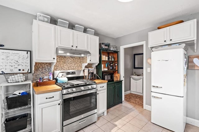 kitchen featuring under cabinet range hood, stainless steel gas range, white cabinets, and freestanding refrigerator