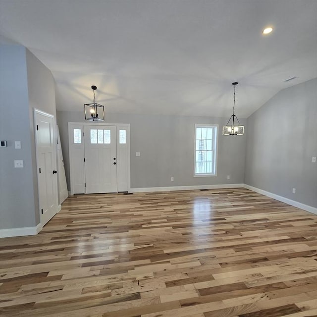 foyer entrance with lofted ceiling, light hardwood / wood-style floors, and a notable chandelier